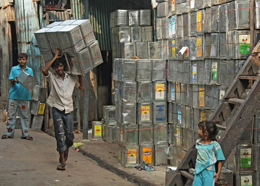 Man carrying tins of cooking oil in a street. 