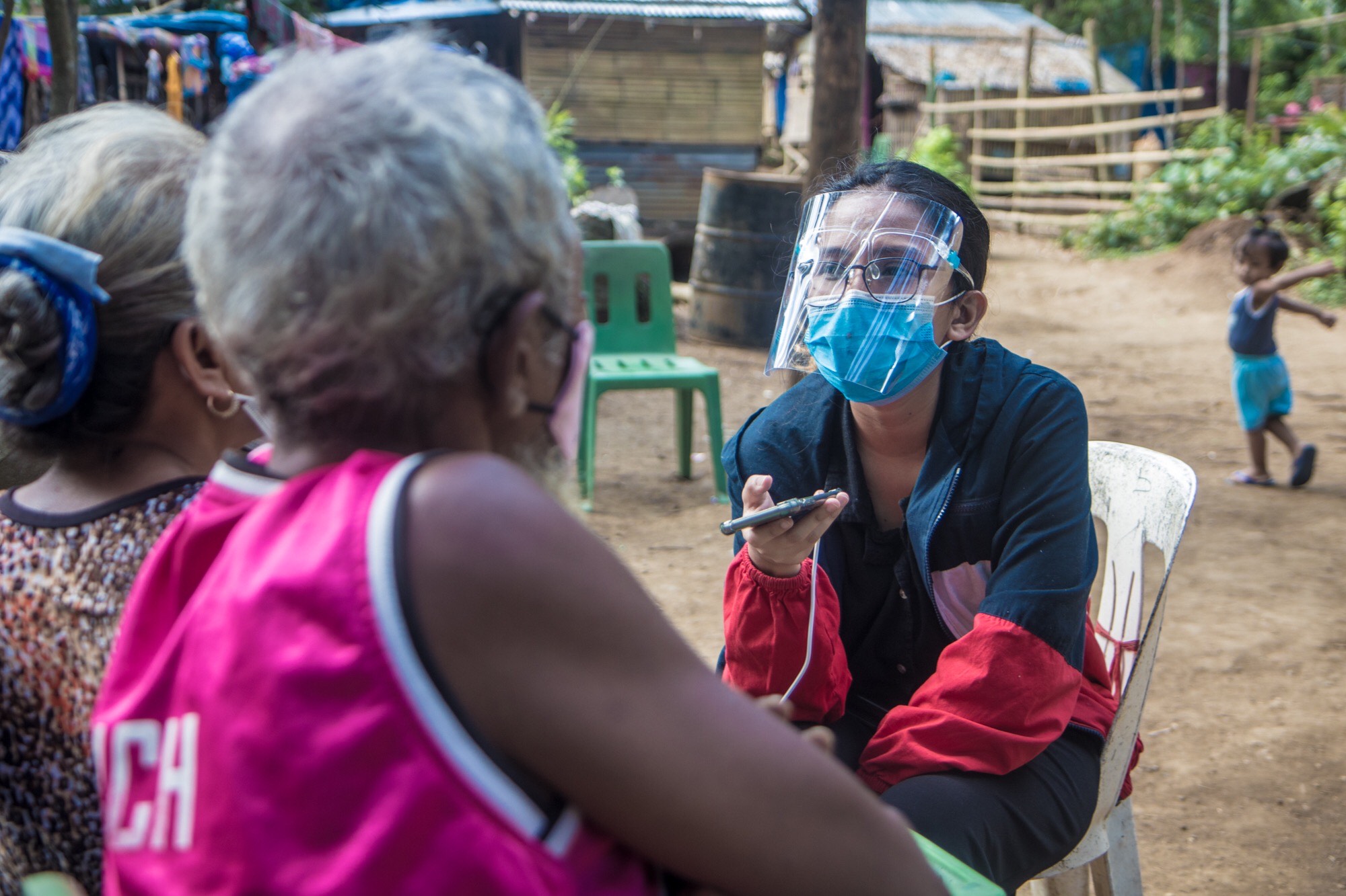 A masked journalist interviews a community elder.
