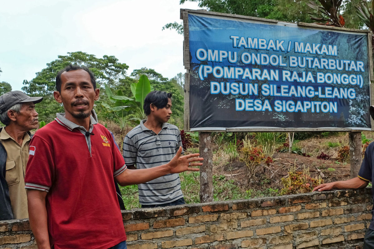 men pointing to indicate the location of the graves of their ancestors next to a sign advertising luxury resort development