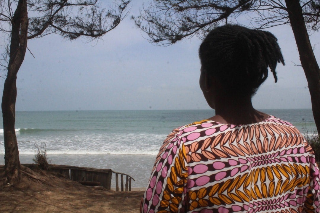 A woman looks out to the ocean from the shore. 
