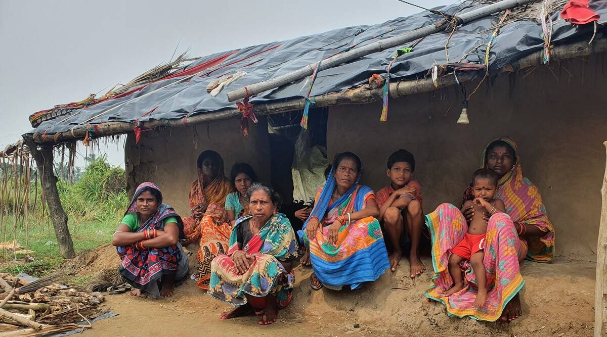 women sit outside a mud hut with their children