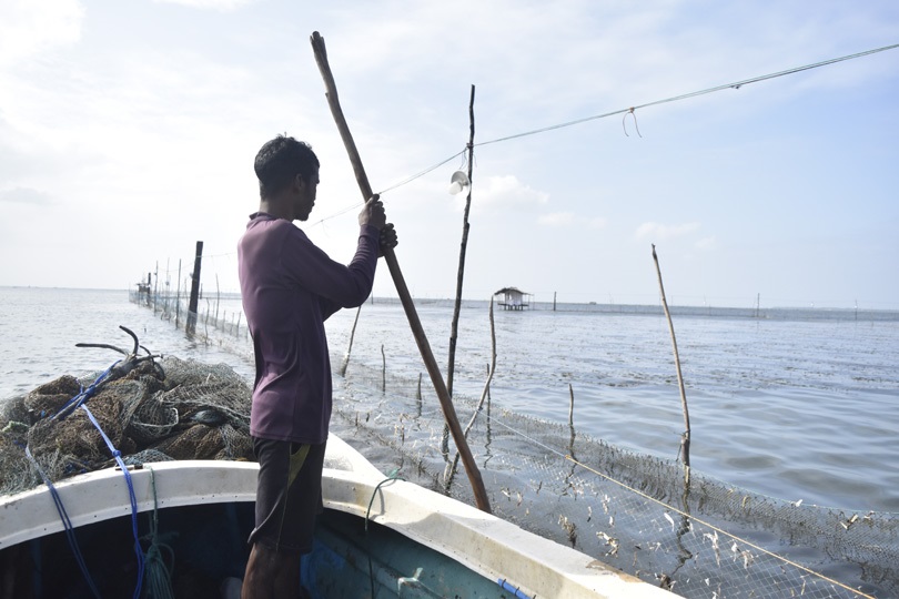 A fisher in Sri Lanka standing on a boat repairing a fishing net