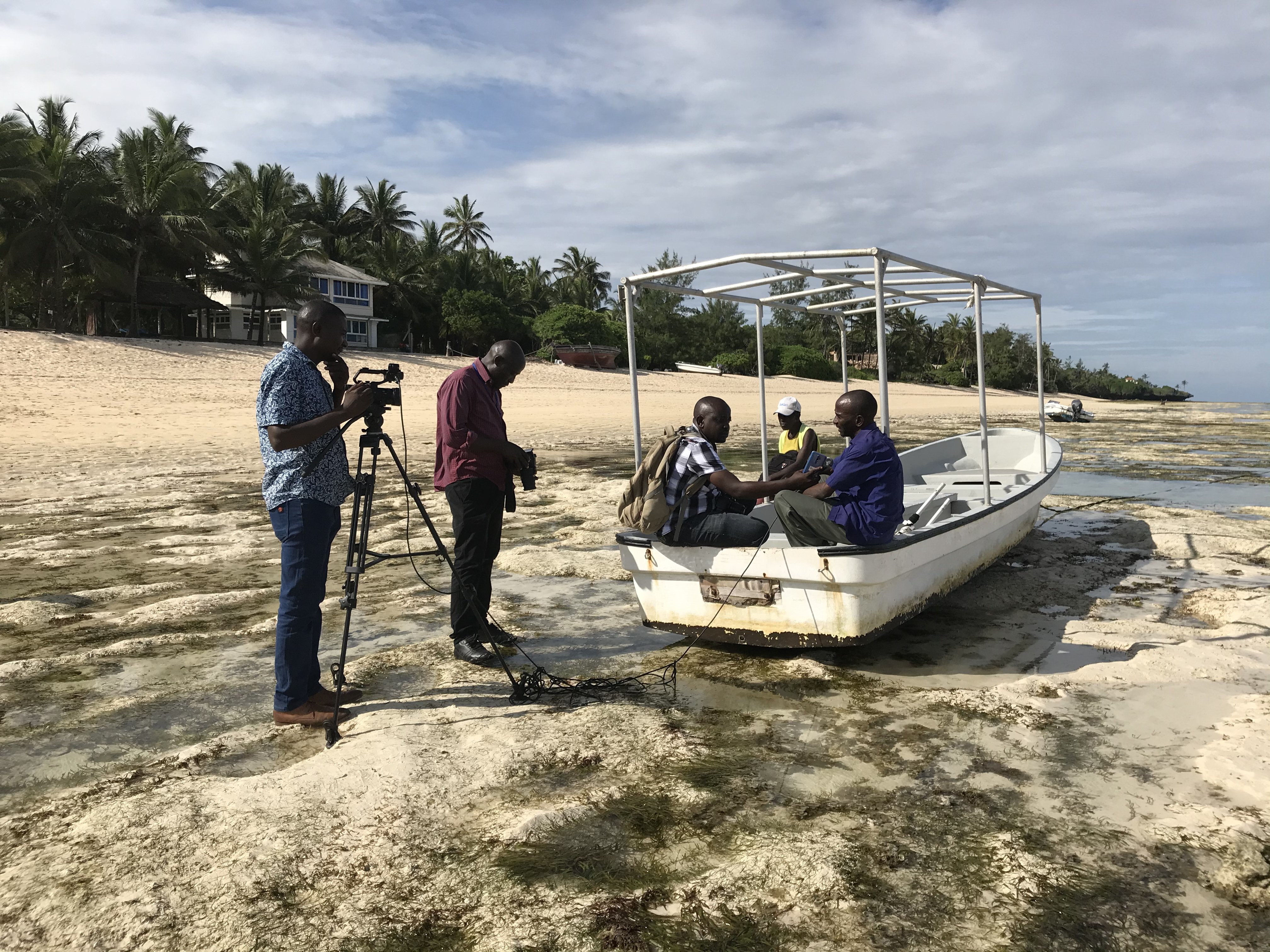 reporters interview men on a fishing boat on the beach