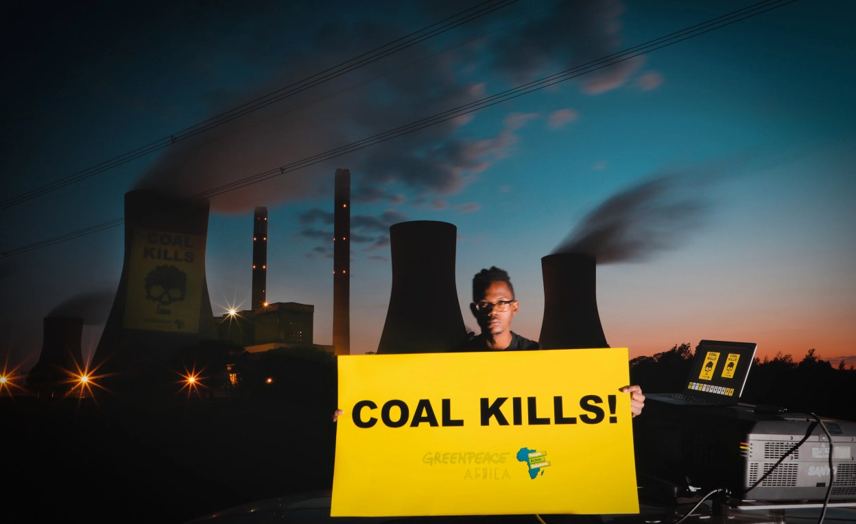 a man holding a sign that says coal kills! with a power plant behind him