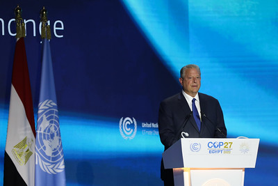al gore standing on stage at a podium with a blue background, giving a speech at cop27