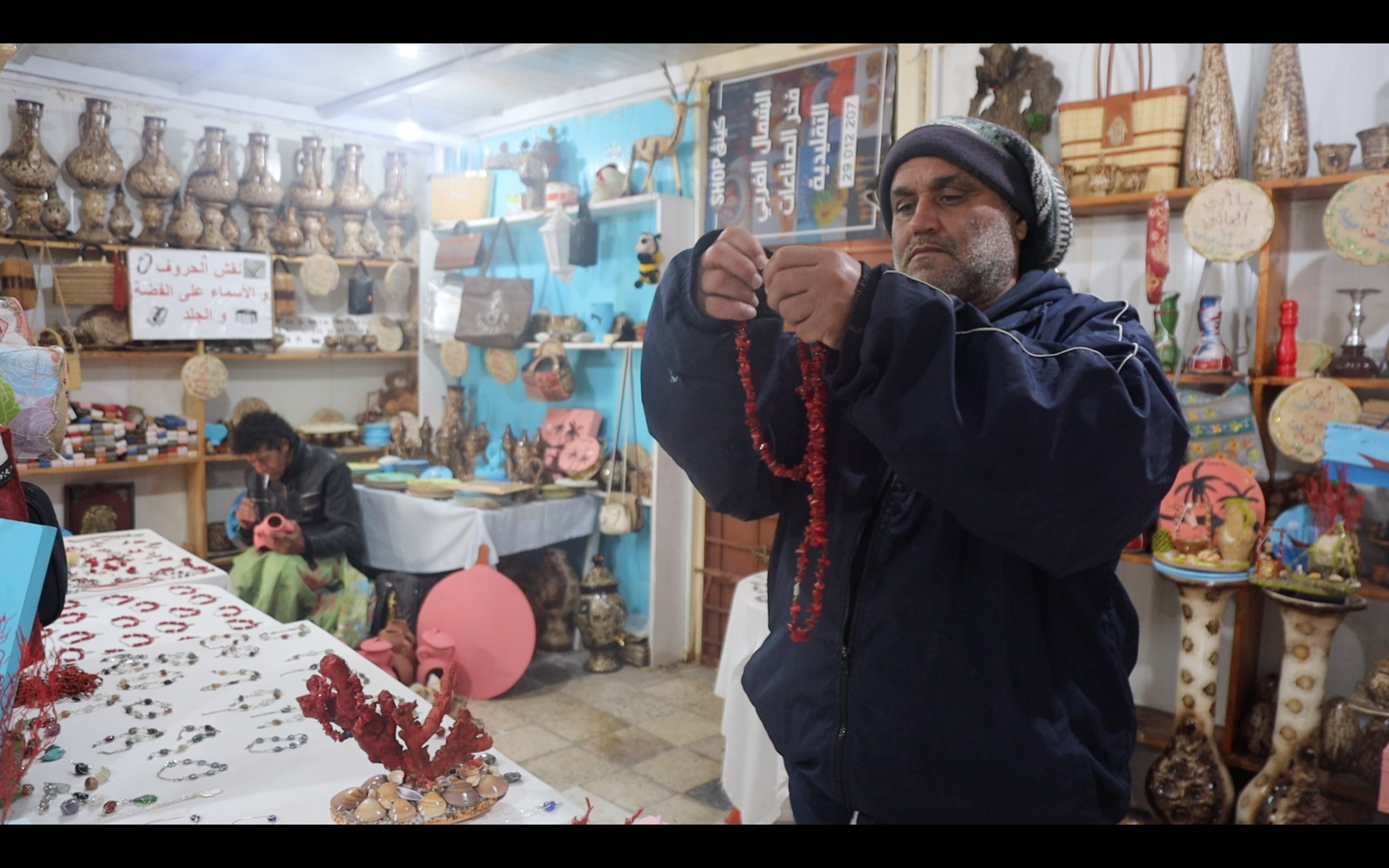 a man in a shop showing a red coral necklace