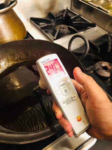 An electronic meter taking a reading over a vat of boiling oil on a stove.
