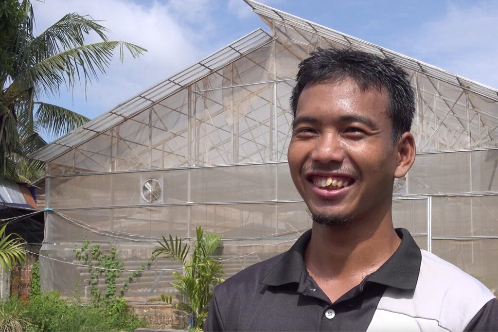 Headshot of smiling man standing in front of a hydroponic farm