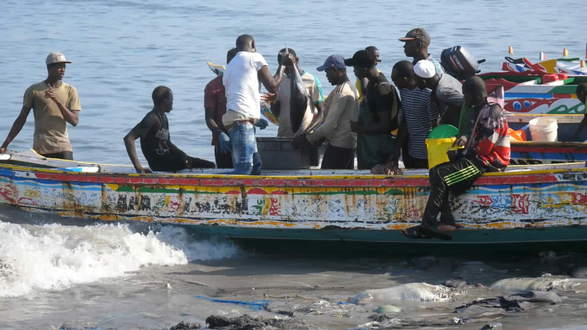 a group of fishermen standing next to a boat at the shore of the beach, unloading fish from inside