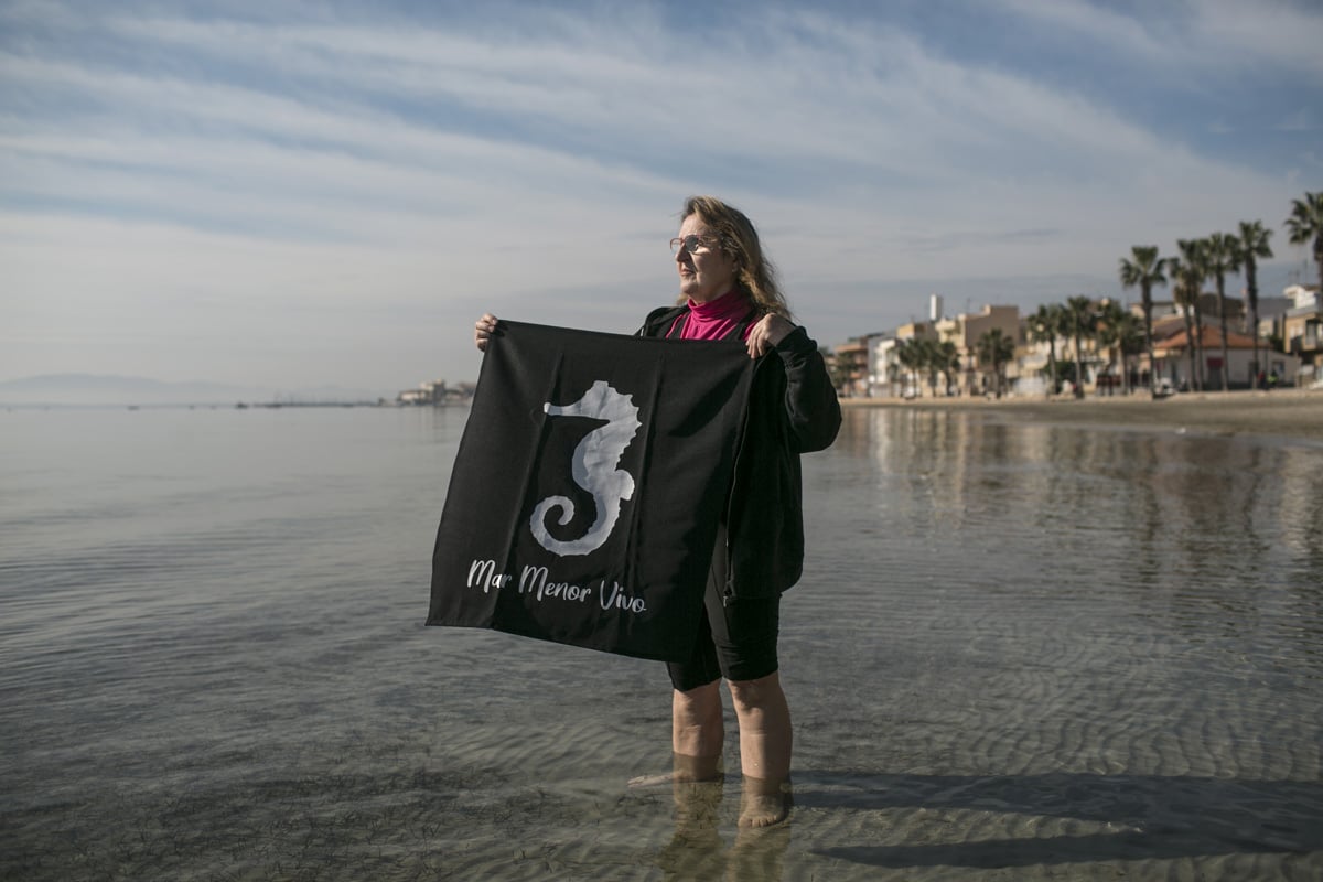 A woman standing in water with a black flag to protest against pollution
