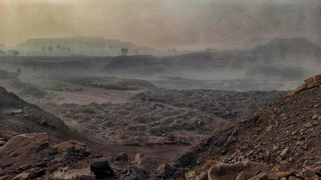 A dusty scene at on open-cast mine, where mounds of coal are debris are neatly assembled