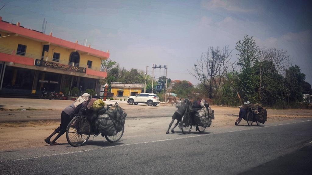 Three men push bicycles laden with blackened gunny bags down the road on a sunny day