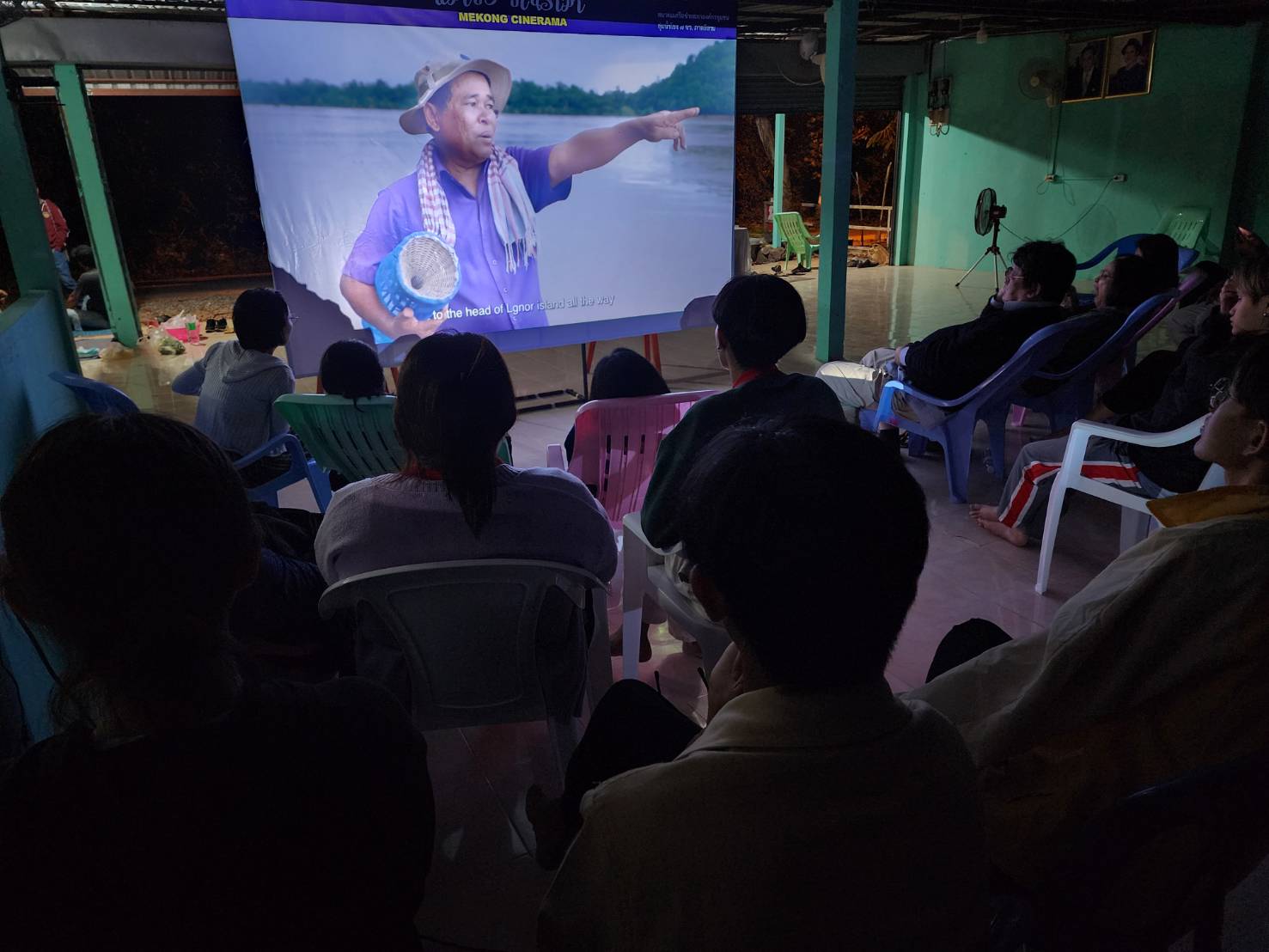 A crowd sits in chairs watching a movie on screen
