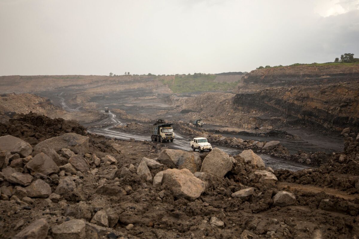 A jeep and truck make their way on muddy paths, laden with bouders on both sides, leading out of an open cast mine.