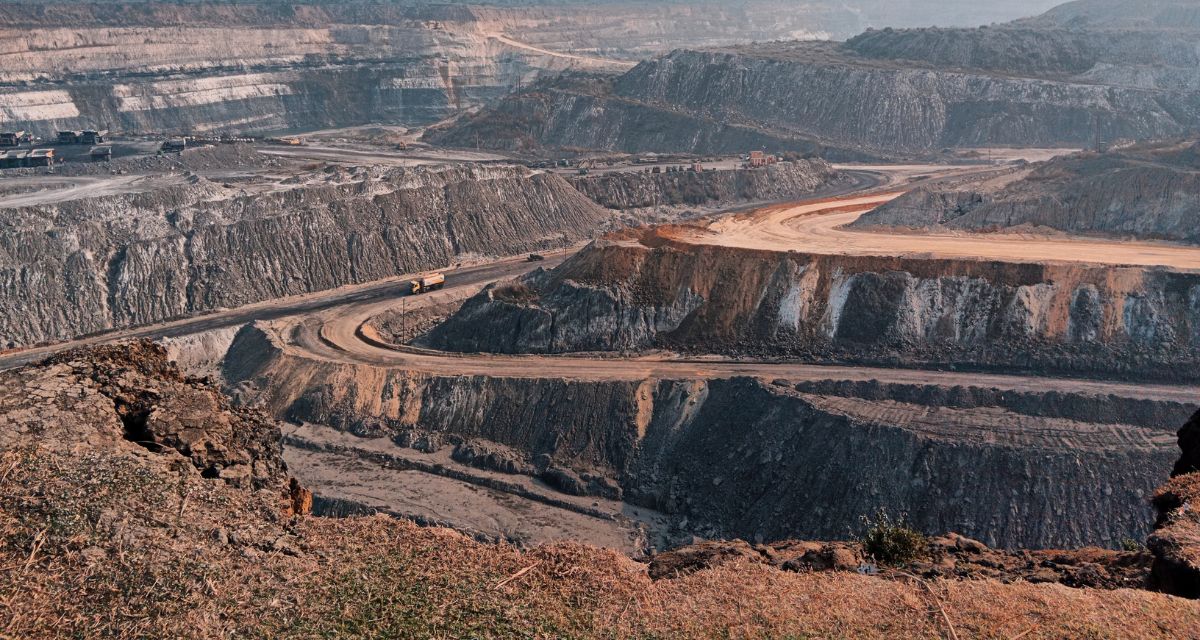 An open-cut coal mine, with some trucks moving down the roughly cut paths