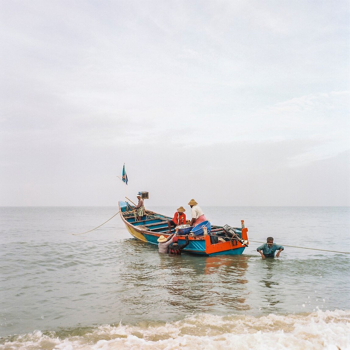 A commercial fishing boat arrives back in the Alleppey harbor. The fisherman sell their catch (likely shrimp, sardines, or mackerel) right off the boat.