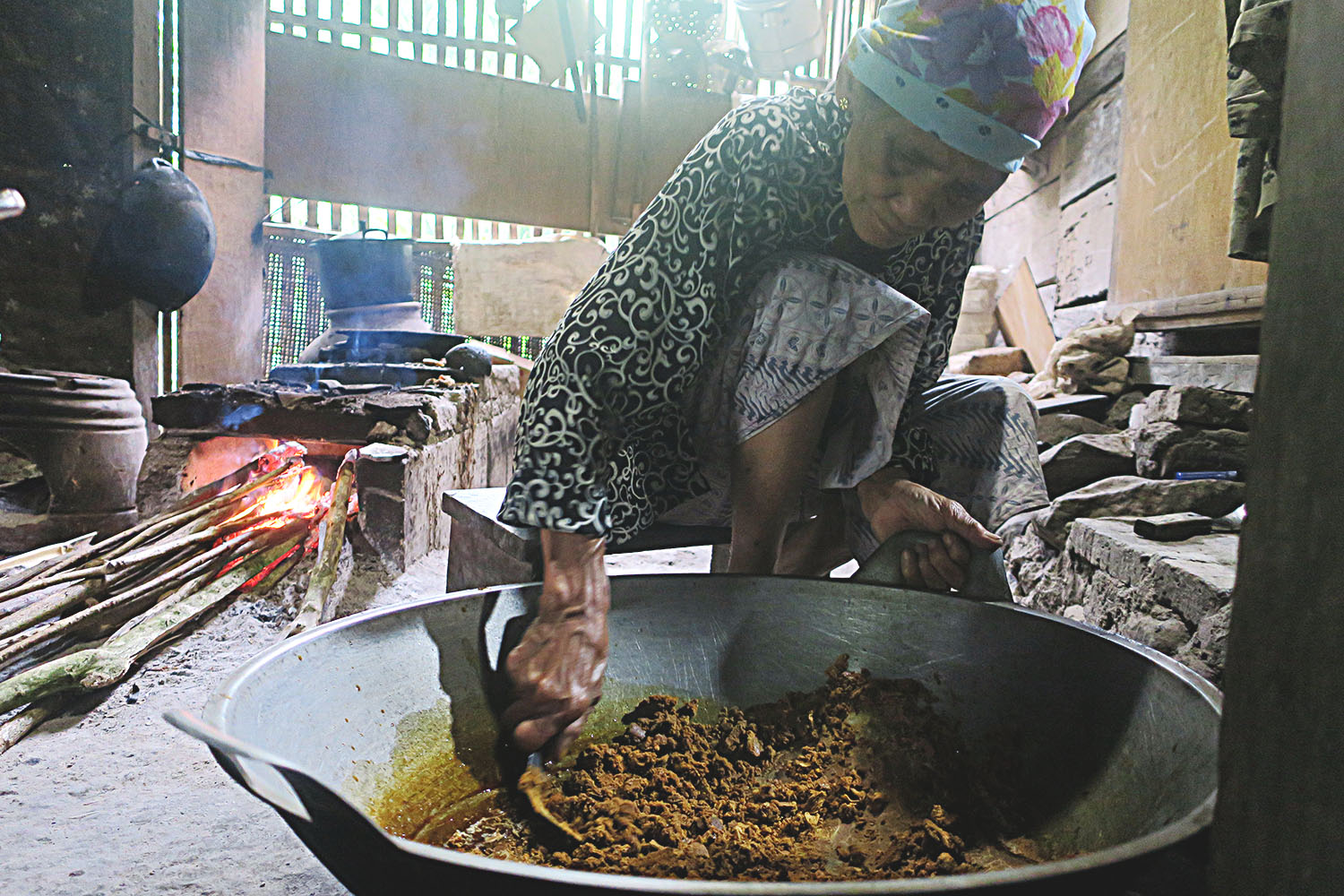 A seated elderly lady making ginger palm sugar.