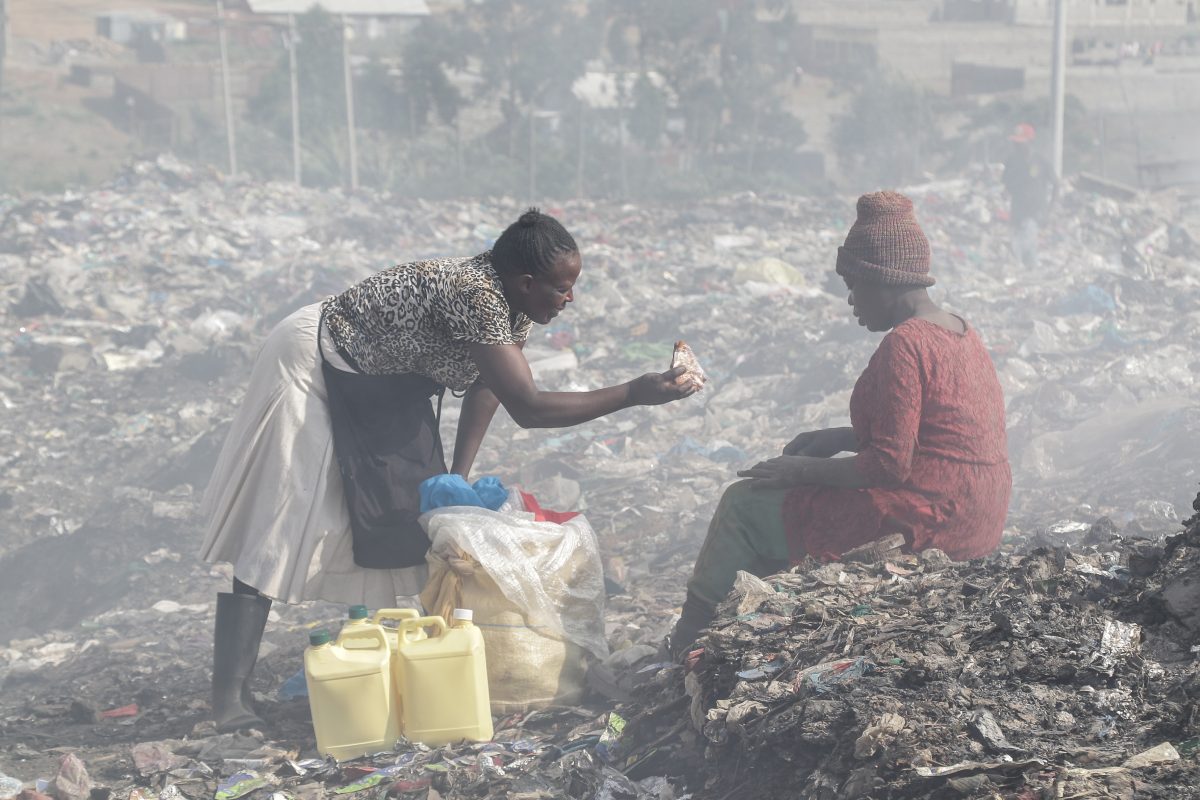 Two women having a conversation while sitting at a garbage dumpsite.