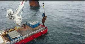 A crane on a vessel lifts containers out of the ocean