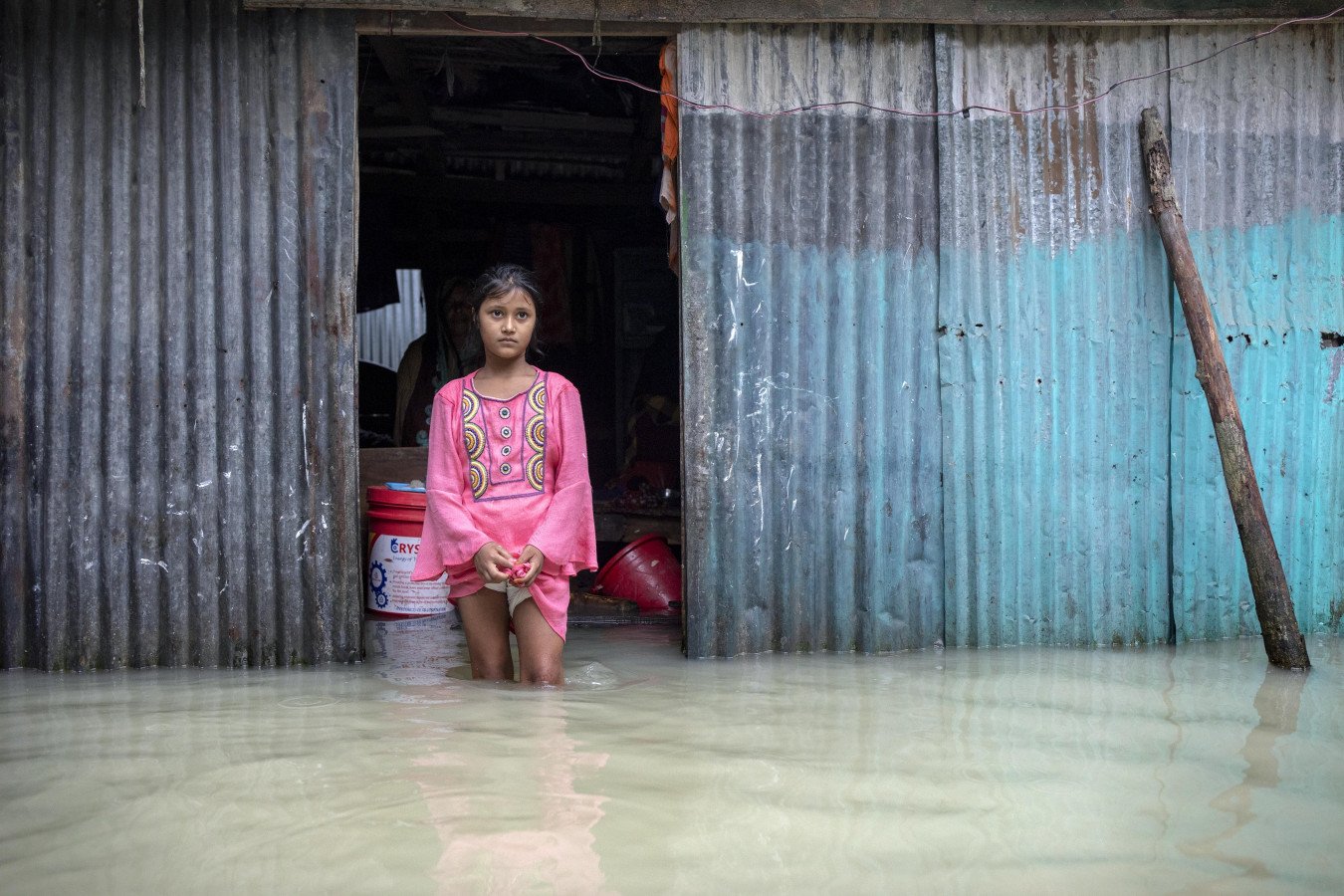  A girl standing outside her flooded home. 