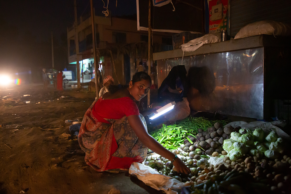 A woman buys vegetables under torchlight in Thirumani village, Pavagada. Villages that leased land to the solar park face regular powercts. Photo by Abhishek N. Chinnappa/Mongabay.