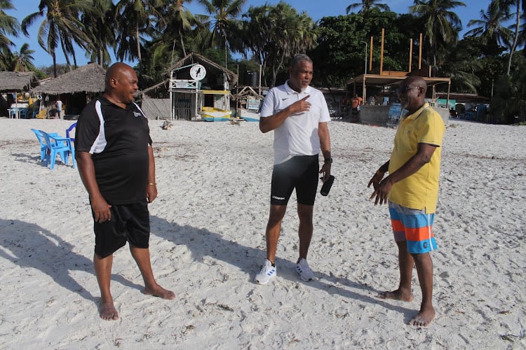 Three men stand chatting on a beach