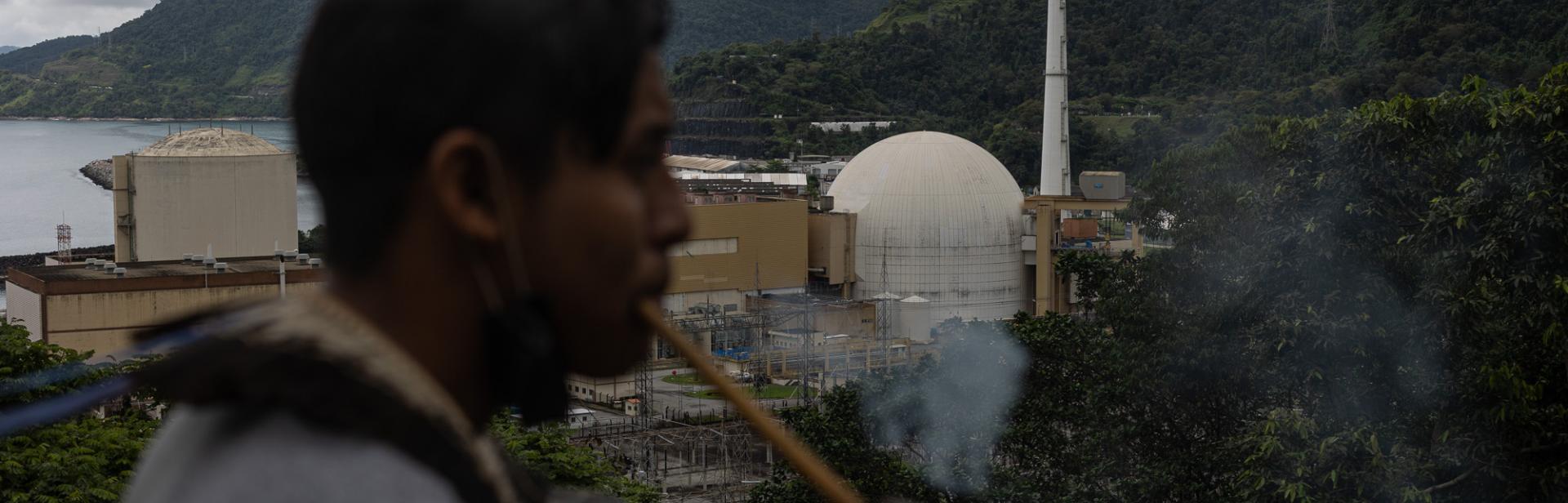 An indigenous man in the foreground, with a nuclear plant in the background