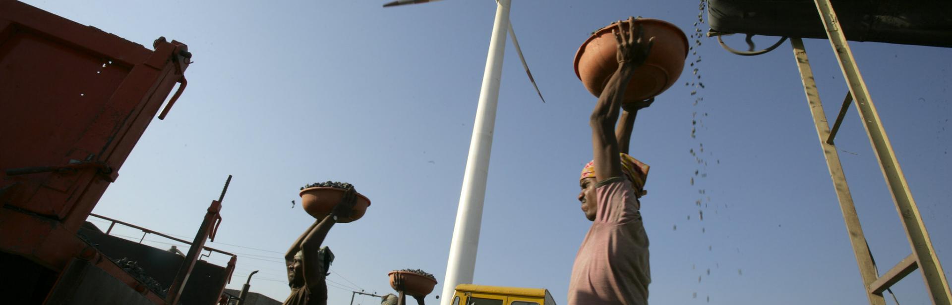 laborers carrying stones with a wind turbine and truck in the background