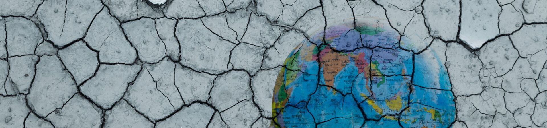 Cracked, dry earth overlays a hand holding a globe