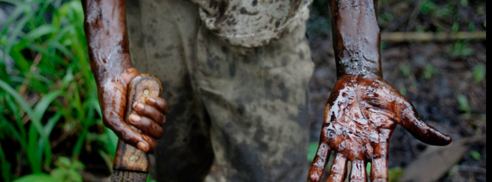 An individual displays his hands covered with oil from the Niger Delta.
