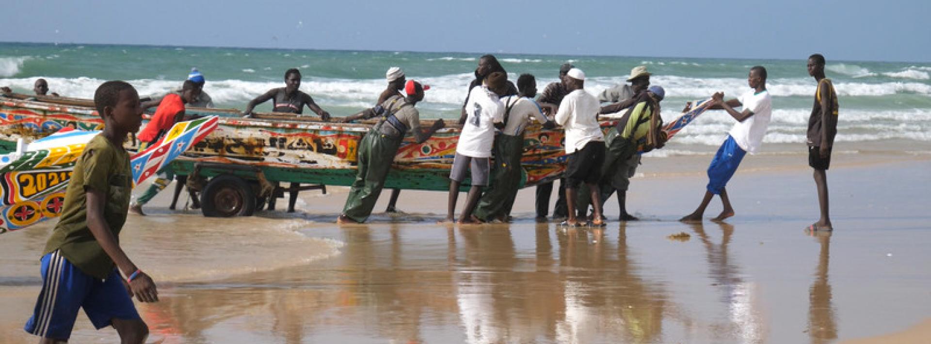 Men grab large fishing boats and pull them onto the shore of the beach in Dakar, Senegal
