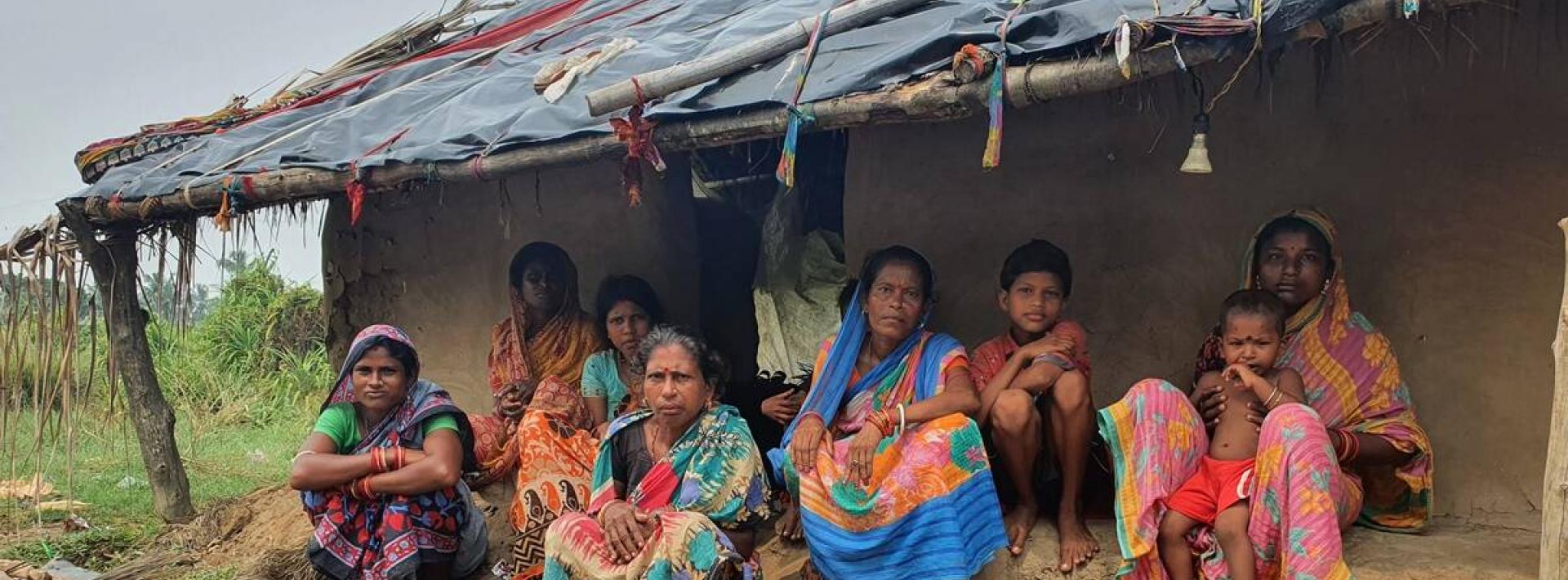 women sit outside a mud hut with their children