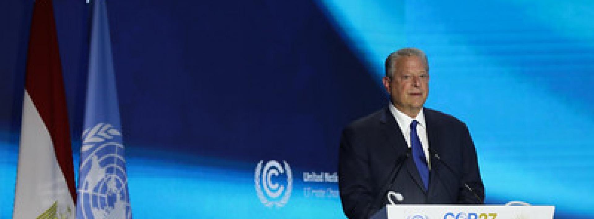 al gore standing on stage at a podium with a blue background, giving a speech at cop27