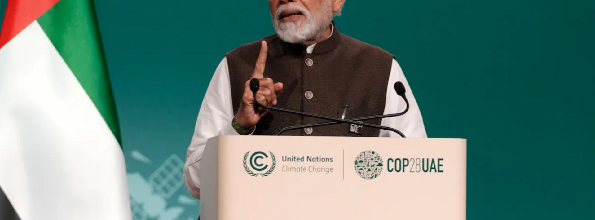 prime minister modi of india speaking at a cop28 pavilion with a green background behind him