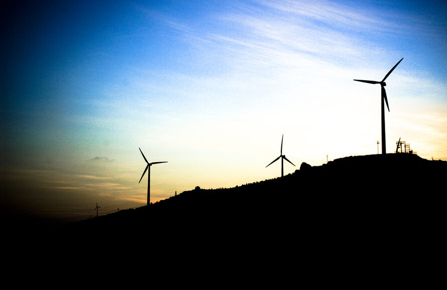 The silhouette of wind turbines on a hill at dusk. 