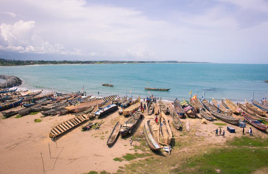 a line of fishing boats sitting on the shoreline with the ocean horizon in the distance