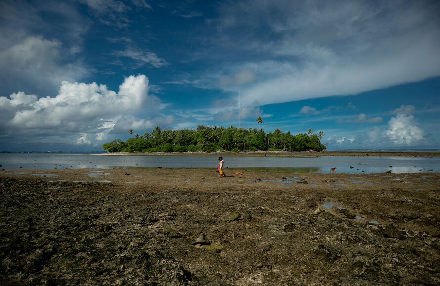two people walking on a deserted shoreline with an island in the background