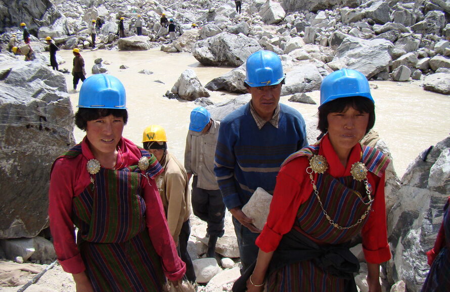 three people in hard hats walk toward the camera with a rocky glacial lake behind them 