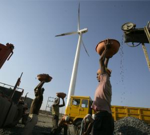 laborers carrying stones with a wind turbine and truck in the background
