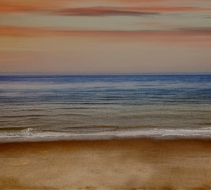 coastal beach view, looking at the waves lapping the shore and the ocean is blue with an orange tint from the sunset in the background