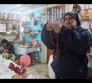 a man in a shop showing a red coral necklace