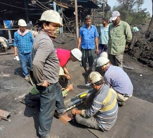 Men in hardhats standing and kneeling at a coal mine.