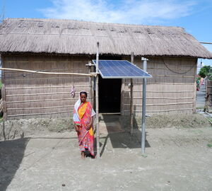a woman stands in front of home that has a solar panel above its entrance