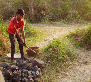 A young boy looks into the camera as he uses a hoe to gather pieces of coal