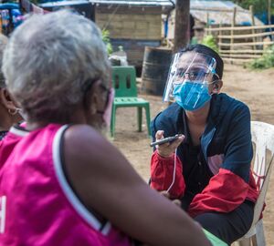 a masked journalist interviews two women outdoors 
