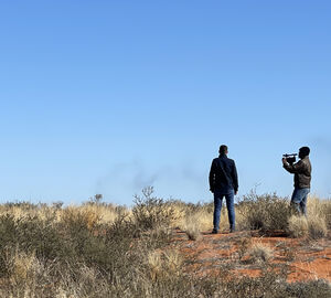 A video journalist films an interviewee and the vast landscape on a sunny day