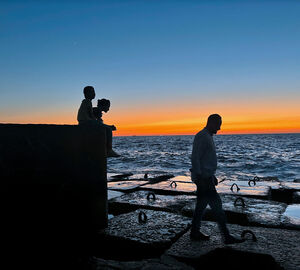 One man and two children on a concrete shore at sunset