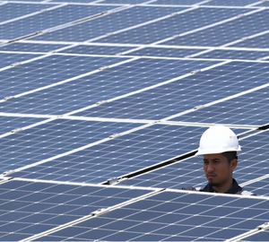 Two workers wearing helmets stand amongst solar panels