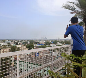 a man stands at a balcony and takes a photo of smoke from a faraway thermal power plant 