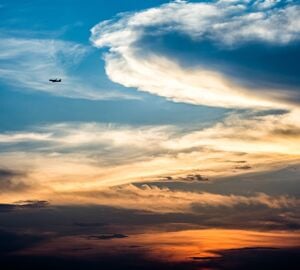 An shot of the sky at sunset with an airplane flying through the clouds